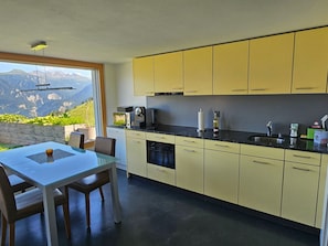 A modern kitchen with yellow cabinets, a black countertop, and a view of mountains through a large window. - im Försterhaus Dalin, (Dalin), by Interhome (Dalin)