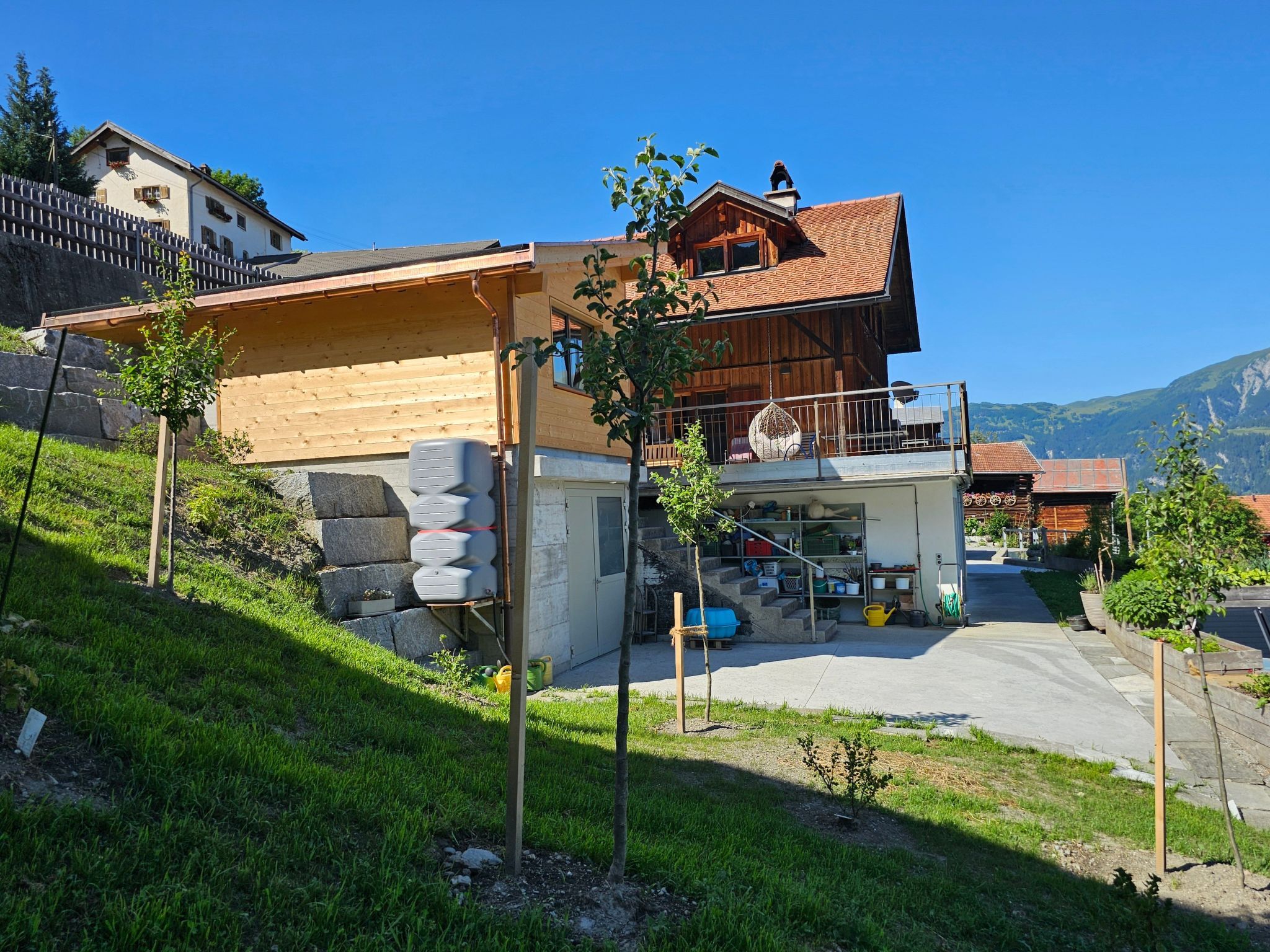 A two-story wooden house with a balcony, a garage, and a stone wall.