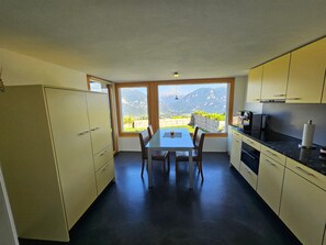 Eine Küche mit Esstisch und Stühlen, großen Fenstern und Blick auf die Berge.