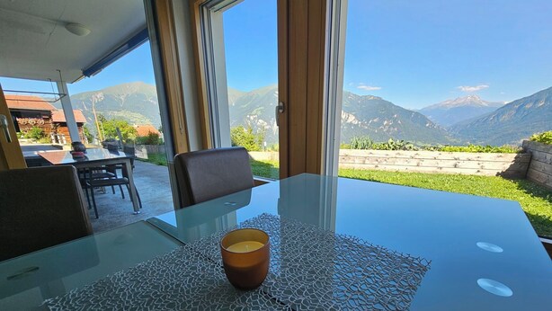 Una mesa de vidrio con un posavasos tejido, una silla y una vela.