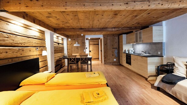 A wooden interior with a bed, a small dining table, and a kitchenette.