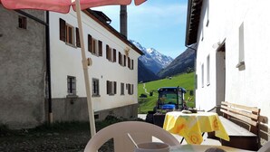 A table with a cup and a stone, a bench, and a view of a tractor on a mountain path.