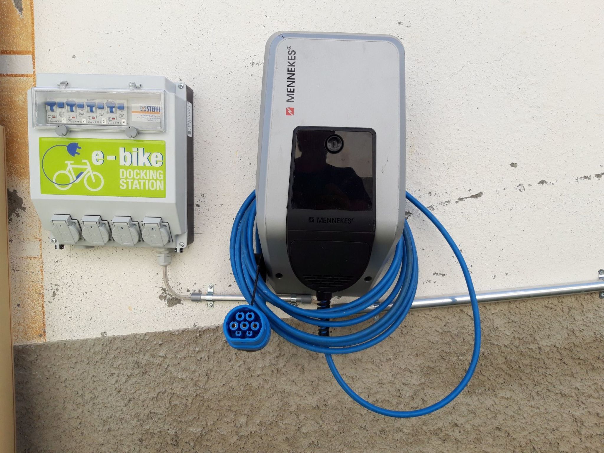 A wall-mounted electric vehicle charging station with a visible plug and a cable connected to it.