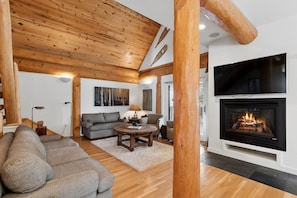 A cozy living room with a fireplace, wooden beams, a sofa, and a television.