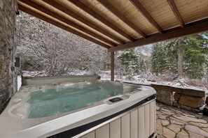 A hot tub under a wooden pergola with a stone wall backdrop. - Ski-in/Ski-out Cabin w/ Sauna and Hot Tub (Whitefish)