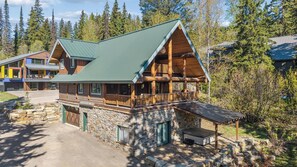 A log cabin with a stone foundation, a green metal roof, and a wooden deck. - Ski-in/Ski-out Cabin w/ Sauna and Hot Tub (Whitefish)