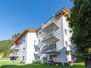 A multi-story building with balconies, a garden area with flowers, and a clear sky. - Mengelt, (Splügen), by Interhome (Splügen)