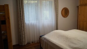 Ein Schlafzimmer mit einem Bett, einem Holzschrank, einem Fenster mit transparenten Vorhängen und einem Spiegel an der Wand.