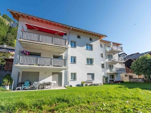 Un immeuble résidentiel à plusieurs étages, doté de balcons, d’un espace extérieur couvert aménagé en coin salon et d’une pelouse bien entretenue.