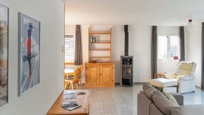Ein modernes Wohnzimmer mit einer Couch, einem Holztisch mit Zeitschriften, einem Bücherregal, einem Kamin und einem Essbereich mit Stuhl und Tisch.