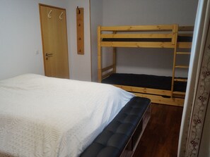 A room with a bunk bed, a single bed, a door, and a wall-mounted coat rack. - Mengelt, (Splügen), by Interhome (Splügen)