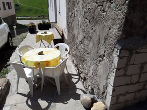 Eine Terrasse mit Tisch und Stühlen, eine Steinmauer und ein geparktes Auto.