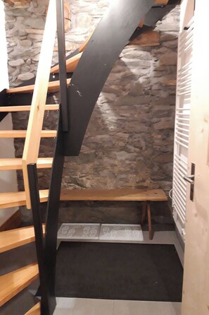 Eine enge Treppe mit einer Holzhandläufe und einer schwarzen Metallstütze, die zu einer Steinmauer führt.