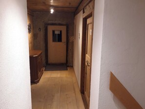 Ein schmaler Flur mit einer Holztür am Ende, einem kleinen Fenster und einem Holzkasten links.