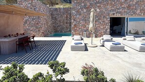 Un espacio al aire libre con paredes de piedra, una piscina, sillones de descanso y una zona de comedor.