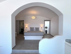 Ein Schlafzimmer mit Bett, Nachttischlampen, einer Topfpflanze und Blick durch eine Bogenöffnung.