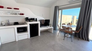 Una cocina moderna con microondas incorporado, cafetera y televisor. Hay un comedor con sillas de mimbre y una mesa, además de un balcón con vistas.