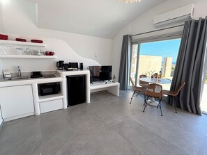 Eine moderne Küche mit integriertem Mikrowellenherd, einer Kaffeemaschine und einem Fernseher. Ein Essbereich mit Korbstühlen und einem Tisch sowie ein Balkon mit Blick sind vorhanden.