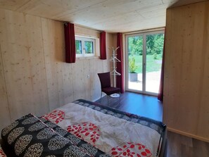 A room with a bed, a chair, a coat rack, and a window with curtains. - Ferienwohnungen Aktien 11, (Sils i.D.), by Interhome (Sils im Domleschg)