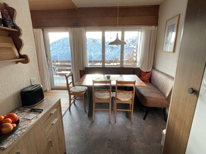 A dining area with a wooden table, chairs, a bench, and a view of mountains through large windows. - Wohnung Ohlenroth-Kalberer, (Sarn-Lescha). by Interhome (Sarn)