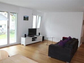 A living room with a TV on a white entertainment unit, a dark sofa with cushions, and a dining table. - Apartment Beeli, (Splügen), by Interhome (Splügen)