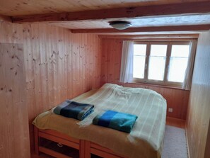 Ein kleines Zimmer mit einem Einzelbett, Holzwänden und einem Fenster.