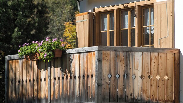 A wooden balcony with a flower pot, a window with a wooden shutter, and a building with a sloped roof. - Ferienhaus Muntschi, (Andeer), by Interhome (Andeer)