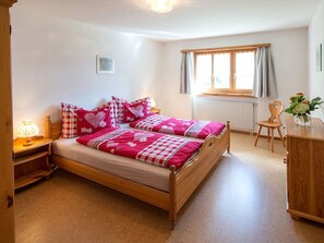 Ein Schlafzimmer mit einem h ölzernen Bett, einem Nachttisch, einem Stuhl, einem Fenster mit Vorhängen und einer Heizung.