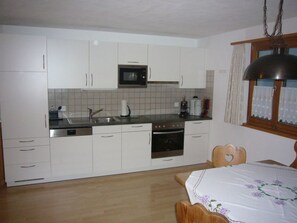 A compact kitchen with white cabinets, a microwave, a sink, and an oven. - Ferienwohnungen Teuriblick A&B, (Splügen), by Interhome (Splügen)