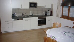 Una cocina con armarios blancos, microondas, cafetera y una mesa de comedor de madera con un corte en forma de corazón.