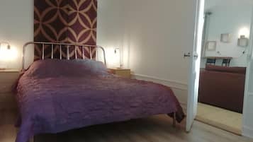 Une chambre à coucher avec un lit, un rideau à motifs, des lampes de chevet et une vue sur une autre pièce.