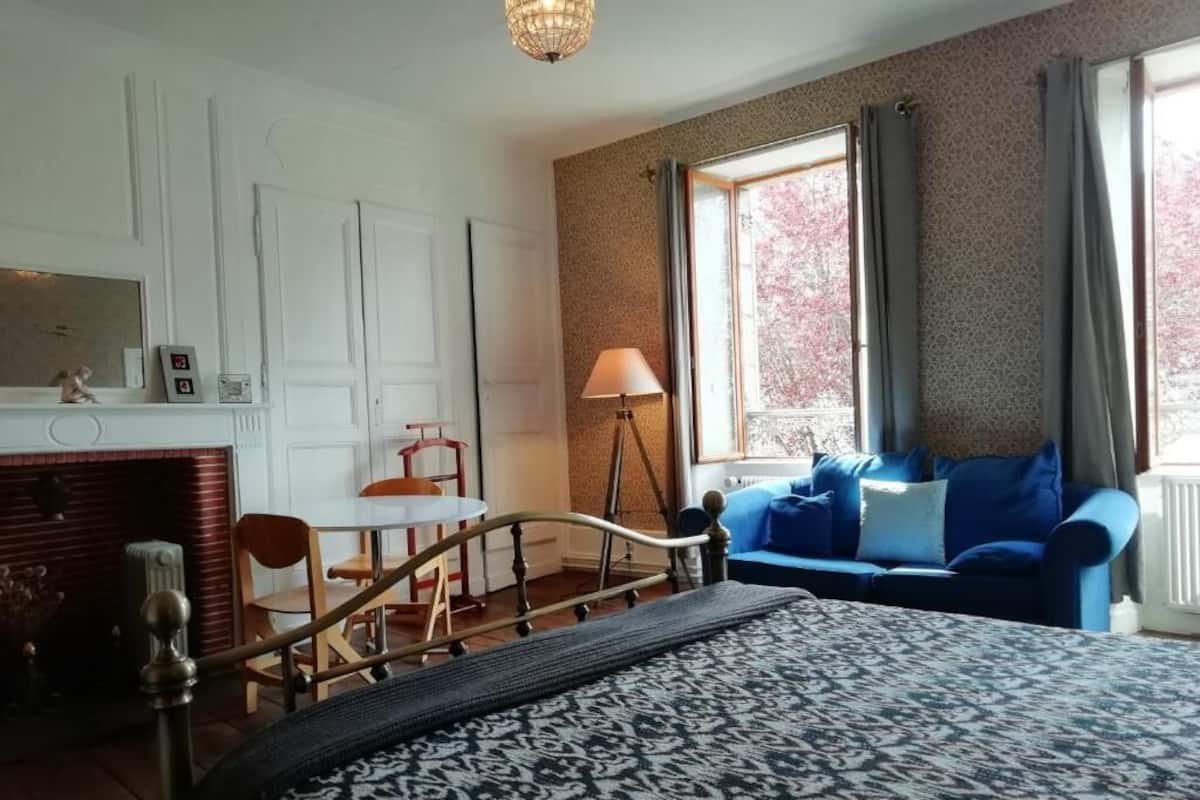 A bedroom with a bed, a desk, a chair, a blue sofa, and a window with curtains.