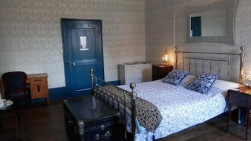 A bedroom with a bed, a dresser, a chair, a desk, a lamp, and a door.