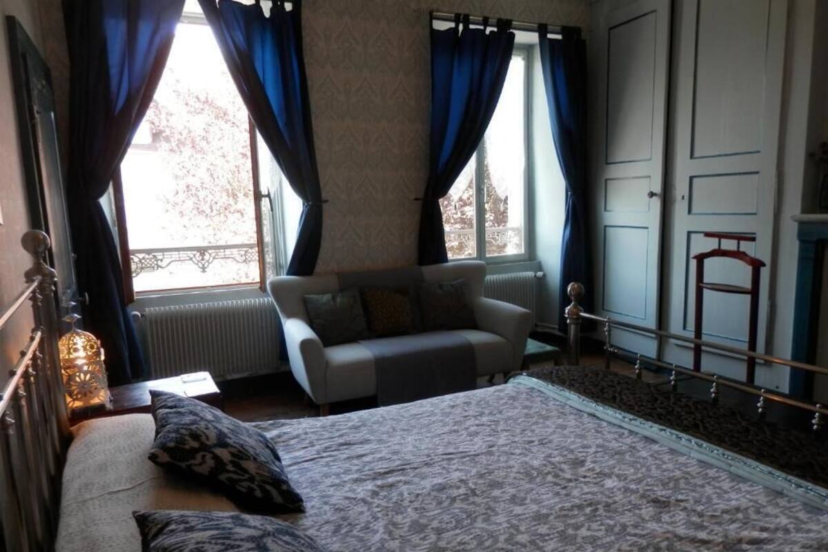 A bedroom with a bed, a sofa, a radiator, a window with curtains, and a wardrobe.