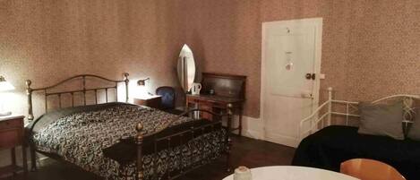 A bedroom with a bed, a bedside table, a chair, a round table, and a door.