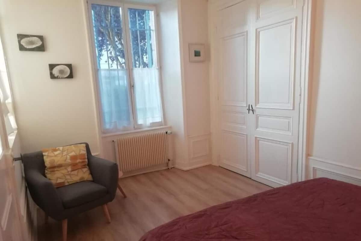A bedroom with a bed, a chair, a window, and a wardrobe.