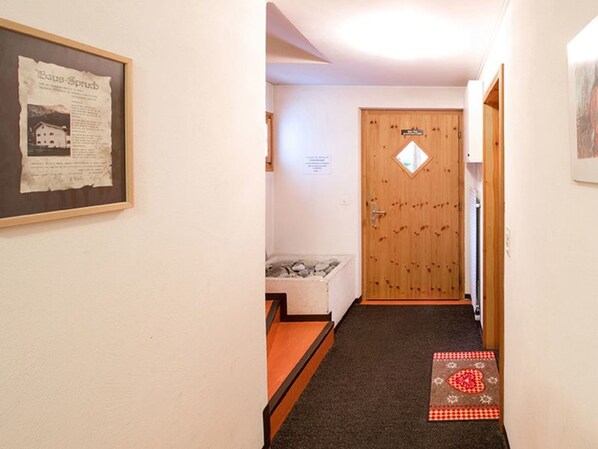 A hallway with a wooden door, a framed notice, and a small bench.