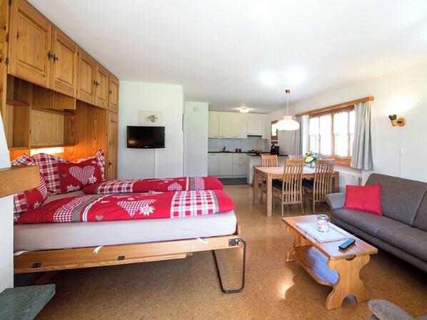 Een kleine kamer met een bed, een bank, een eettafel en een televisie.