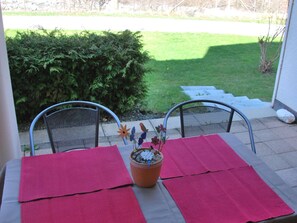 A patio with two metal chairs, a table with a red tablecloth, and a potted plant with decorative elements. - Wohnung Sut Baselgia, (Andeer), by Interhome (Andeer)