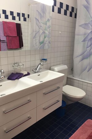 A bathroom with a white sink, two drawers, a mirror, a toilet, and a shower curtain with a floral pattern. - Wohnung Sut Baselgia, (Andeer), by Interhome (Andeer)