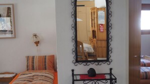 A bedroom with a bed, a bedside table, a mirror, and a small shelf with a decorative item.