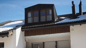 Um edifício de dois andares com uma varanda, chaminé e telhado coberto de neve.