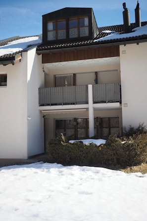 Ein zweistöckiges Gebäude mit Balkon, Schornstein und verschneitem Dach.