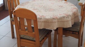 A dining area with a round table, four wooden chairs, and a floral tablecloth.