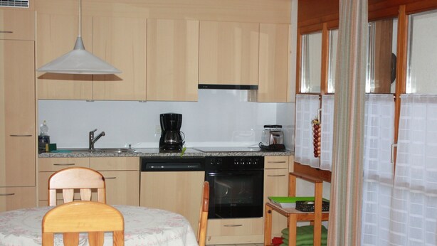 A kitchen with wooden cabinets, a dishwasher, a stove, a coffee maker, and a dining table with chairs.