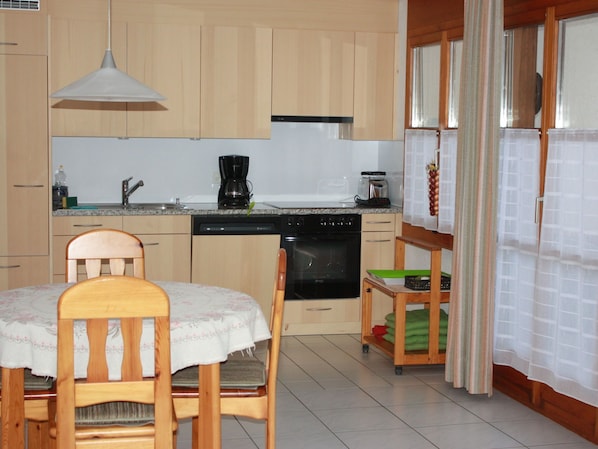 A kitchen with wooden cabinets, a dishwasher, a stove, a coffee maker, and a dining table with chairs. - Wohnung Sut Baselgia, (Andeer), by Interhome (Andeer)