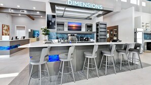 Ein moderner Barbereich mit Check-in-Schalter, Barhocker und einem Fernsehbild mit Sonnenuntergang.