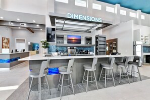 A modern bar area with a check-in counter, bar stools, and a television screen displaying a sunset. - Elevated Luxe Condo near Disney with Resort & Waterpark Access - B42-247 (Kissimmee)