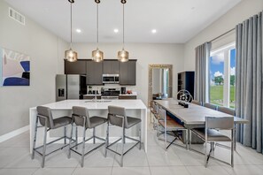 A modern kitchen with a central island, bar stools, pendant lighting, and a dining area with a long table and chairs. - Elevated Luxe Condo near Disney with Resort & Waterpark Access - B42-247 (Kissimmee)