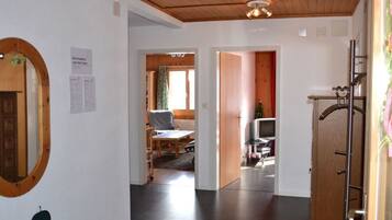 Ein Korridor mit Holzboden, einem Spiegel und einem Kleiderständer. Eine Tür führt zu einem Zimmer mit einem Bett und einem Fernseher.